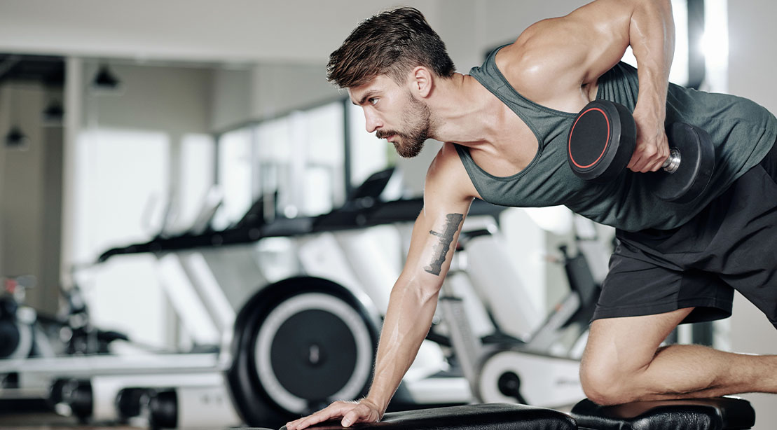 Fit and muscular man performing a dumbbell row for his triset workout for strength and endurance