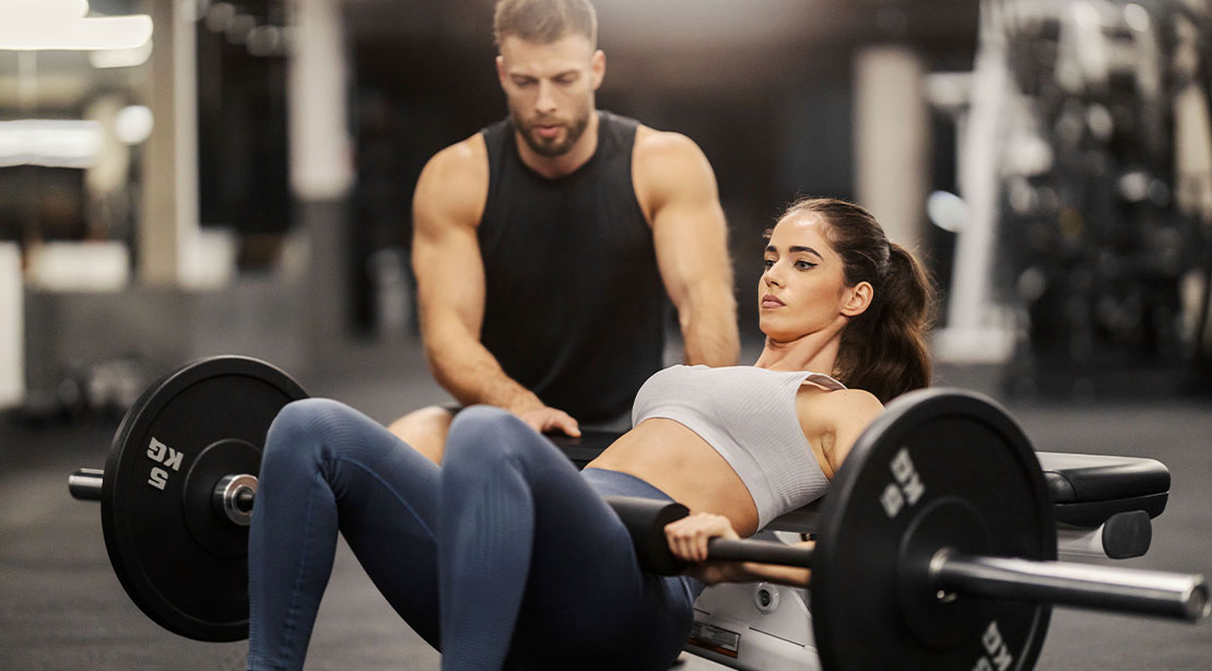 Male fitness trainer teaching his client how to perform a hip thrusters correctly